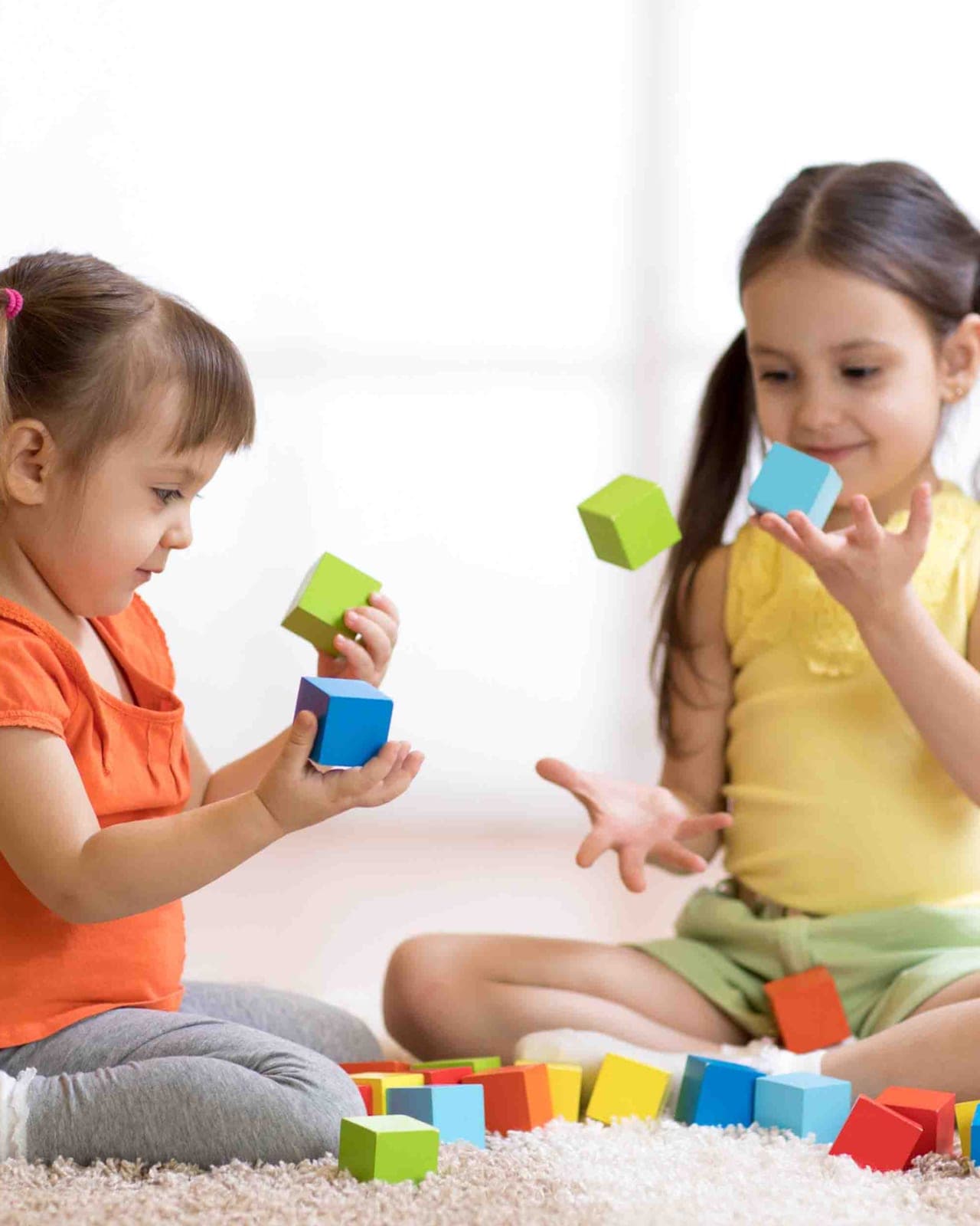 Two young girls playing with wooden blocks on a freshly cleaned carpet in a Sugar Land, TX home
